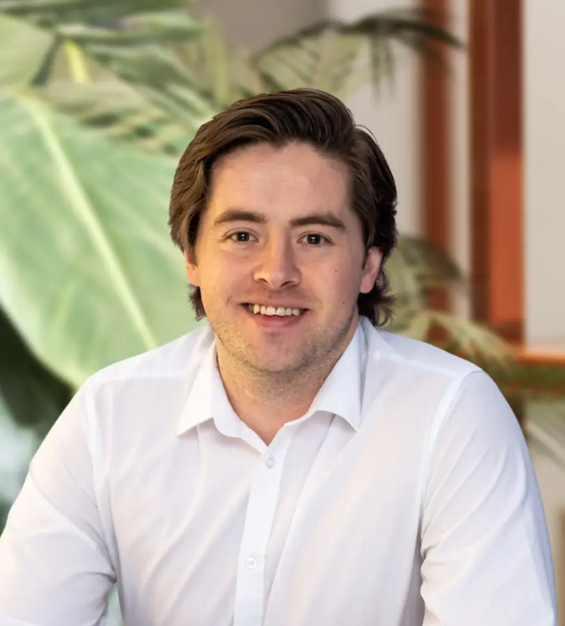 A man with brown hair smiles. He is wearing a white shirt