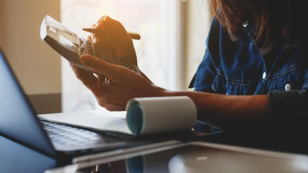 A woman uses a calculator and laptop to work out payroll