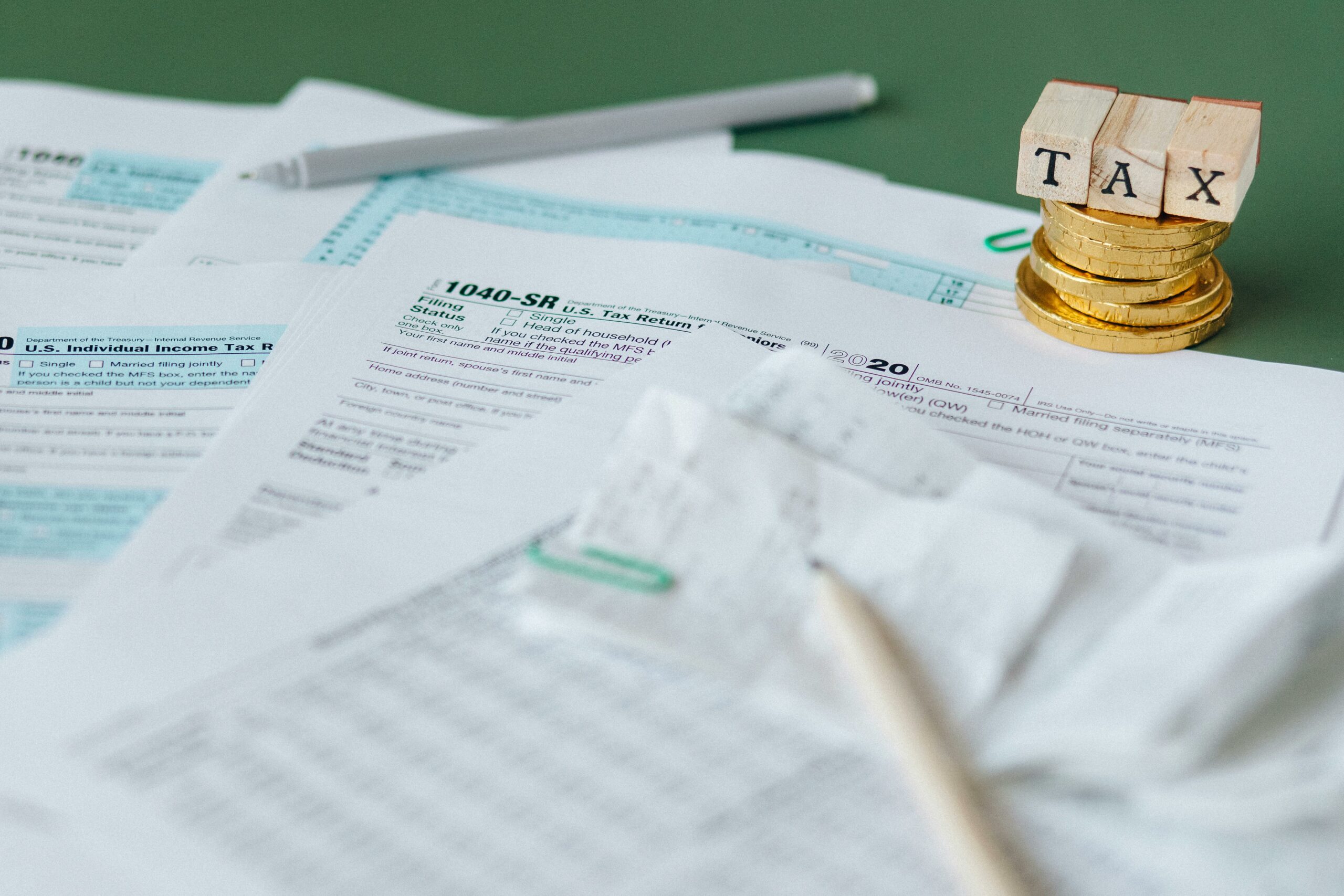 A pile of tax forms, a stack of British pound coins and wooden blocks that spell out "tax".