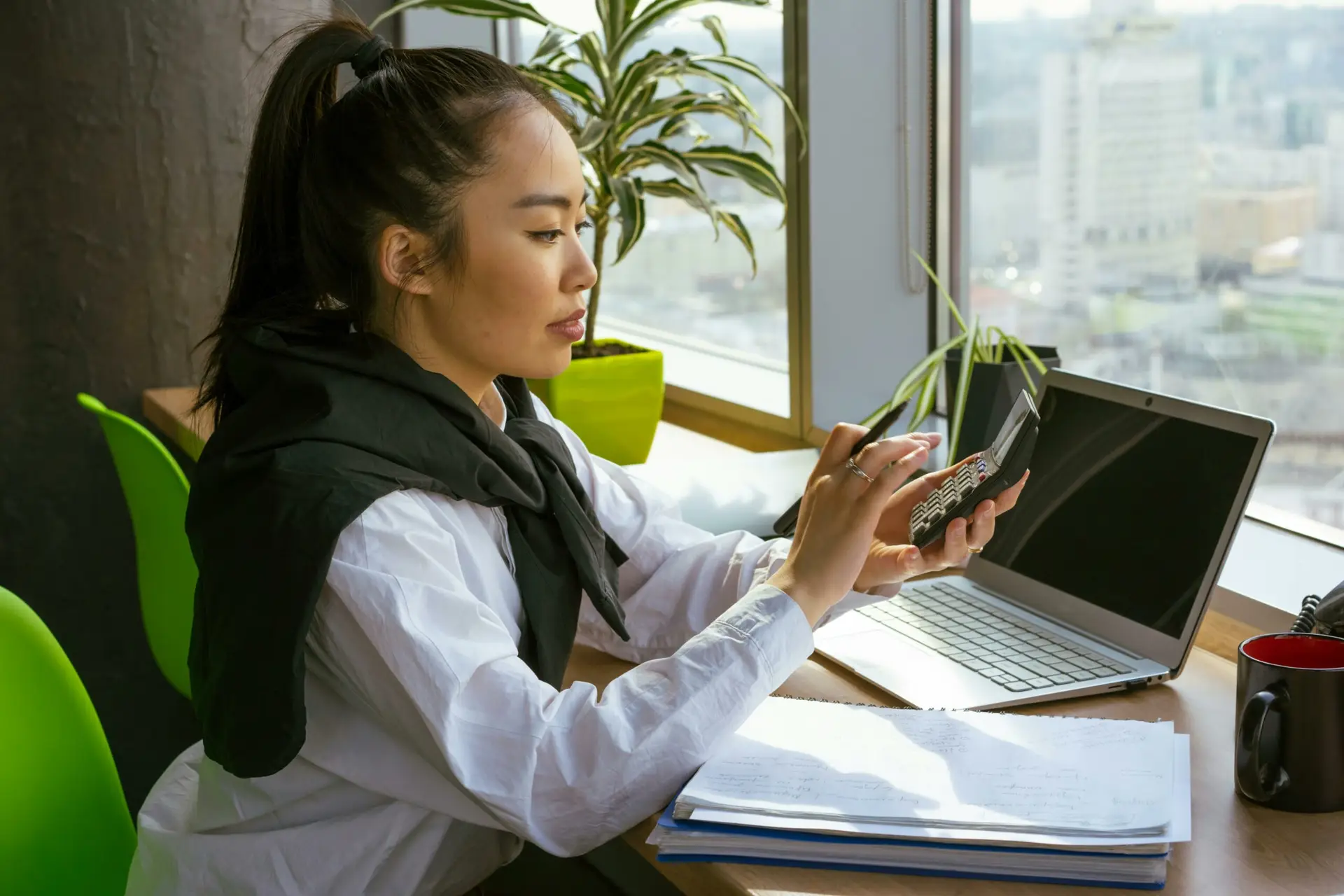 A woman sat at a desk with an open laptop, typing on a calculator.