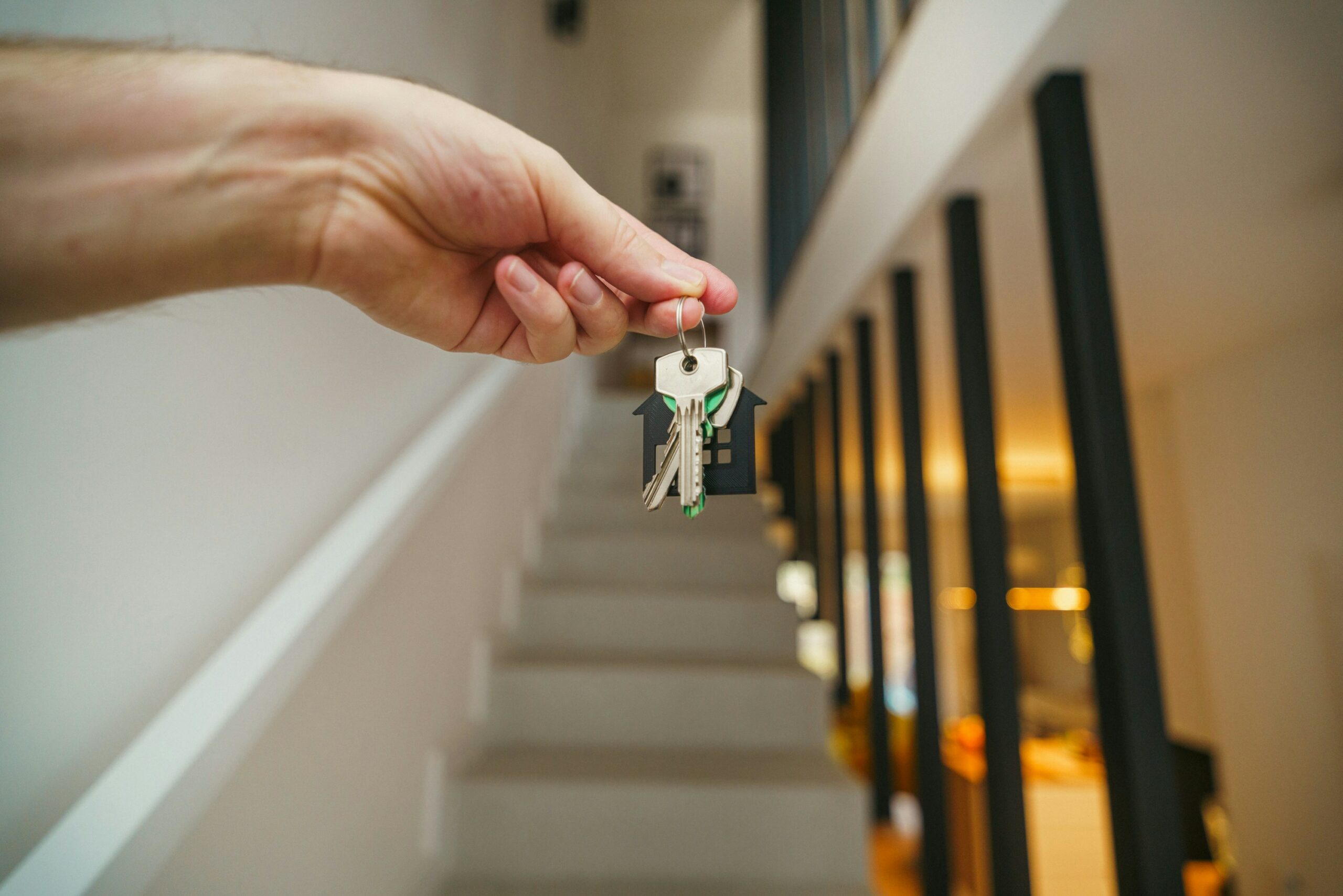 A person holding house keys in front of a staircase in a hallway